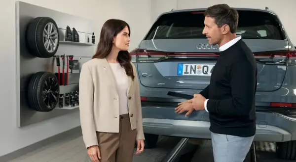 Klientka rozmawia z pracownikiem serwisu Audi o akcjach serwisowych. Na ścianie widoczne opony i akcesoria.