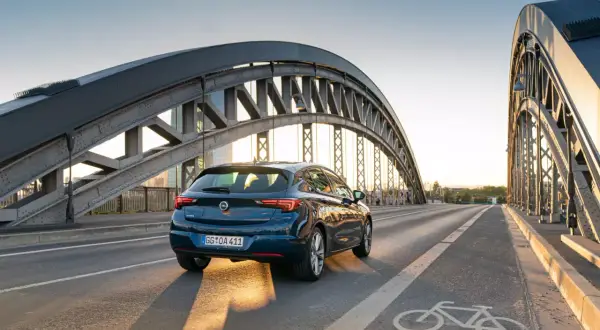 Ciemnoniebieska Astra jedzie po moście pod zachodzącym słońcem. Dostępne akcje serwisowe Opel dla Twojej Astry.