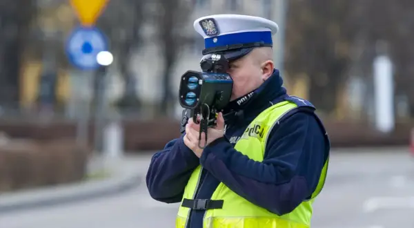 Policjant w kamizelce odblaskowej mierzy prędkość pojazdu. Uważaj na przekroczenie prędkości!