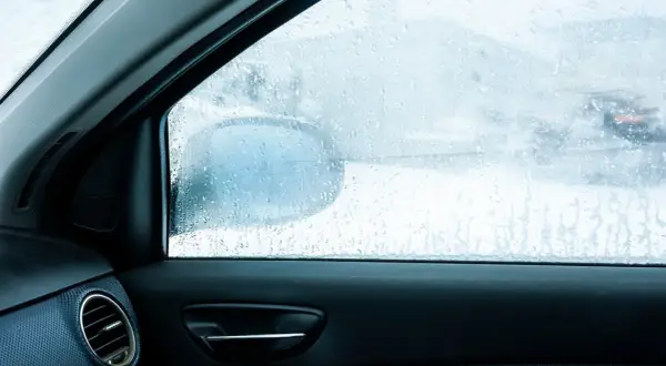 Widok z wnętrza auta na zaparowane szyby. Krople wody na szybie utrudniają widoczność drogi i lusterka bocznego.