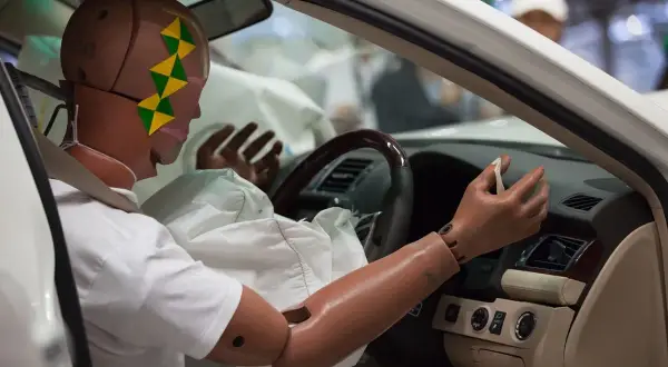 Manekin w samochodzie po teście zderzeniowym. Wystrzelone poduszki powietrzne otaczają manekina, budząc pytanie, czy wystrzelone poduszki dyskwalifikują auto.
