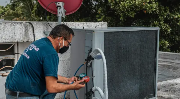 Technik sprawdza klimatyzację, która nie wydaje zimnego powietrza z nawiewu. Na dachu budynku, obok anteny satelitarnej, naprawia urządzenie.