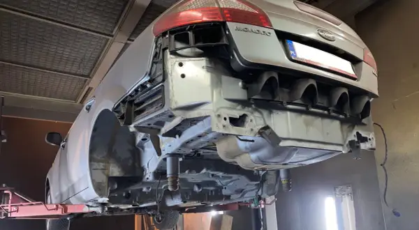 Ford Mondeo na podnośniku, przygotowany do piaskowania podwozia. Widać gołe elementy konstrukcyjne i usunięty zderzak.