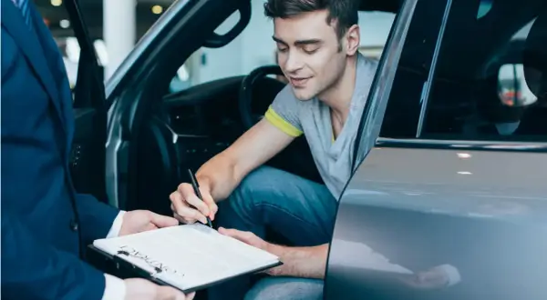 Mężczyzna w samochodzie podpisuje umowę. Chcesz wiedzieć, jak sprawdzić, czy auto jest w leasingu? Dokumenty są kluczem.