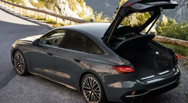 Szary Audi RS 6 Avant, czyli liftback co to, z otwartym bagażnikiem na górskiej drodze.