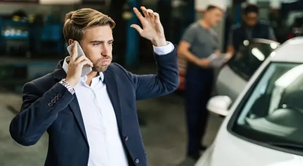 Mężczyzna w garniturze rozmawia przez telefon, martwiąc się o ubezpieczenie samochodu w leasingu.