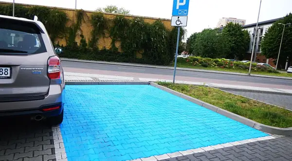 Niebieski, specjalny obszar do parkowania na miejscu dla niepełnosprawnych. Obok znak drogowy P i symbol wózka inwalidzkiego.