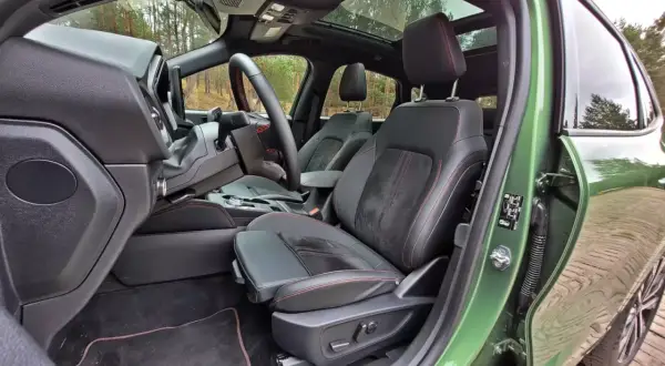 Wnętrze Ford Kuga z czarną tapicerką i czerwonymi przeszyciami. Widok na fotel kierowcy, deskę rozdzielczą i fragment dachu panoramicznego.