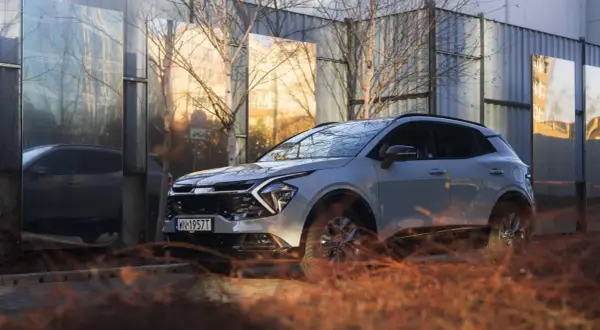 Nowe auto typu SUV w jasnym kolorze, zaparkowane obok lśniących paneli odbijających otoczenie.