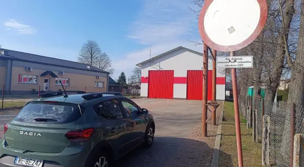 Zielony Dacia Sandero stoi przed remizą OSP. Znak zakazu ruchu z tabliczką "Nie dotyczy pojazdów OSP i pojazdów członków OSP" ostrzega przed mandatem.