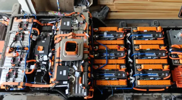 Widok z góry na budowę baterii samochodu elektrycznego, z widocznymi modułami ogniw, pomarańczowymi przewodami i czarnymi skrzynkami sterującymi.