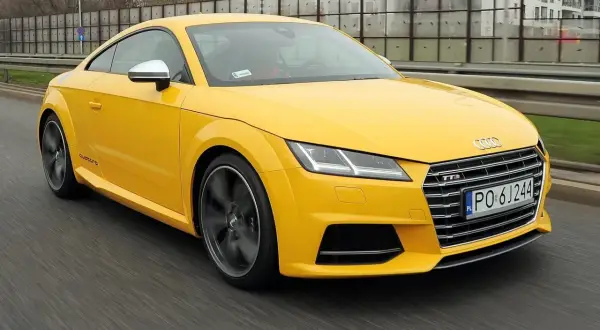 Żółte Audi TT RS, jedna z nowszych audi tt generacji, pędzi po drodze.