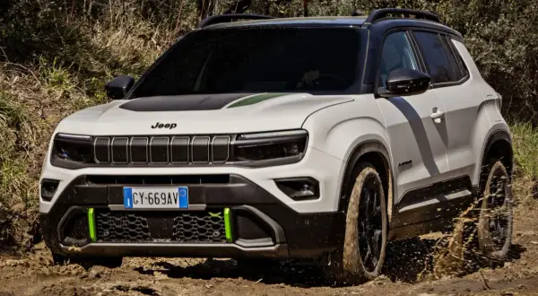 Biały terenowy SUV Jeep z zielonymi akcentami pokonuje błotniste wyzwanie, chlapiąc wodą.