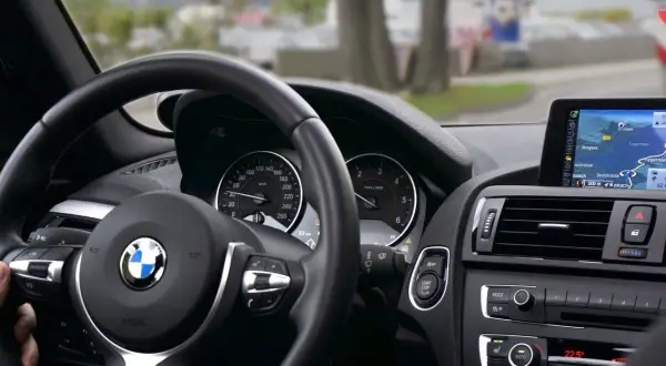 Wnętrze BMW z widokiem na kierownicę i nawigację. Rozważasz wynajem samochodu osobowego a VAT? Sprawdź szczegóły.