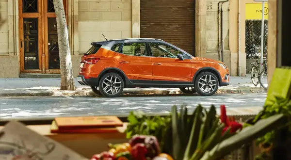 Pomarańczowy suv, crossover, zaparkowany na ulicy w mieście, obok drzewa i budynku.