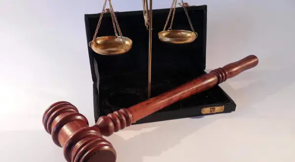 Młotek sędziowski i waga szalkowa leżą obok otwartego czarnego etui. Waga wygląda na lekko przechyloną, co może sugerować uszkodzenie mechaniczne lub nierównowagę.