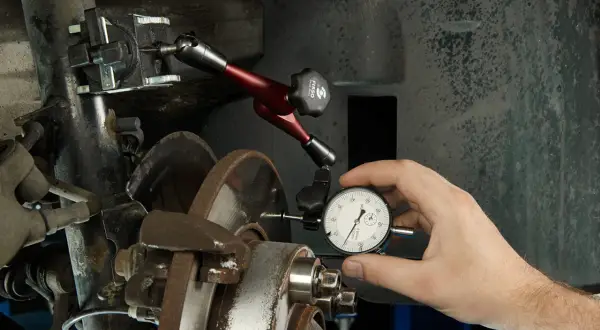 Mechanik mierzy bicie tarczy hamulcowej, aby zdiagnozować drgania kierownicy przy hamowaniu.