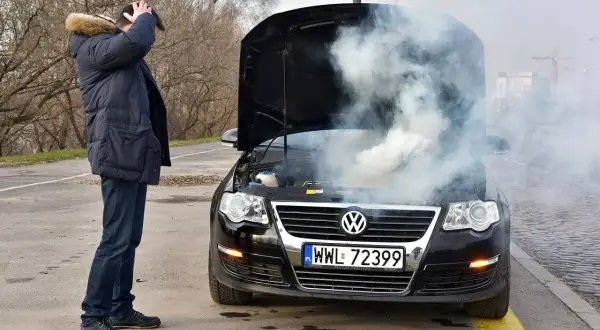 Mężczyzna z przerażeniem patrzy na dym spod maski i czuje zapach spalenizny. Awaria Volkswagena na drodze.