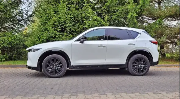 Biała Mazda CX-5 na tle zieleni. Zastanawiasz się nad jej spalaniem? Ten SUV oferuje świetny kompromis między osiągami a ekonomią.