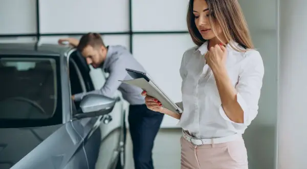Kobieta z tabletem analizuje ofertę leasingu finansowego, podczas gdy mężczyzna ogląda nowy samochód.