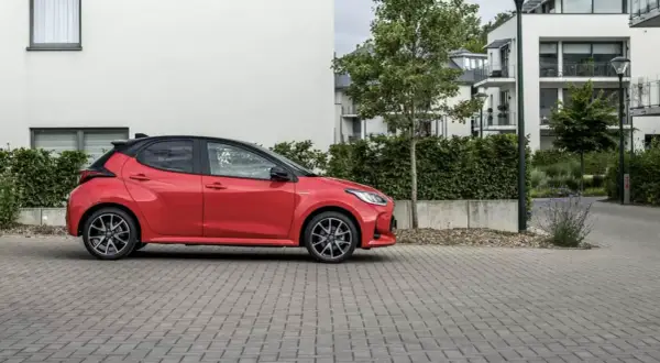 Czerwone, małe, niezawodne auto stoi na brukowanym podjeździe przed nowoczesnym budynkiem.