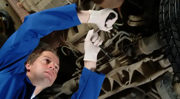 Mechanik w białych rękawiczkach dokręca śrubę pod samochodem. Może to być związane z objawami wybitych tulei tylnej belki.