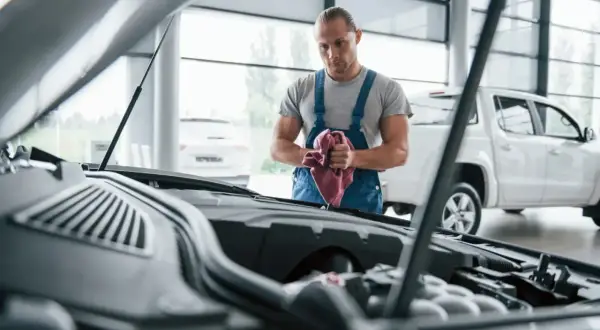 Mechanik w warsztacie z ręcznikiem w dłoniach. Zastanawiasz się, kto płaci VAT za naprawę samochodu w leasingu? Sprawdź szczegóły.
