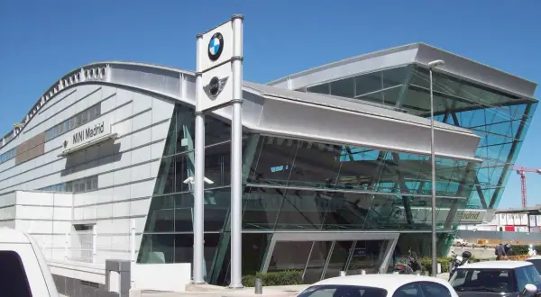 Nowoczesny salon MINI Madrid z logo BMW. W tle widać budynek i dźwig budowlany, a przed nim zaparkowane samochody, gotowe do akcje przywoławcze BMW.