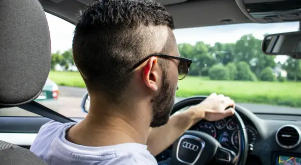 Mężczyzna w okularach przeciwsłonecznych prowadzi Audi. Zastanawia się, ile mam czasu na ubezpieczenie samochodu po zakupie, by móc legalnie jeździć.