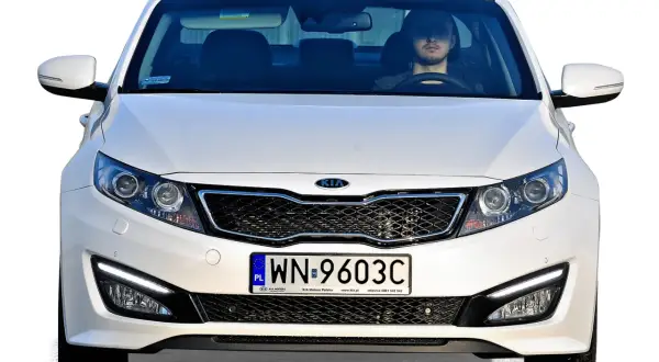 Białe auto z Korei Południowej, model Kia, z młodym kierowcą za kierownicą.