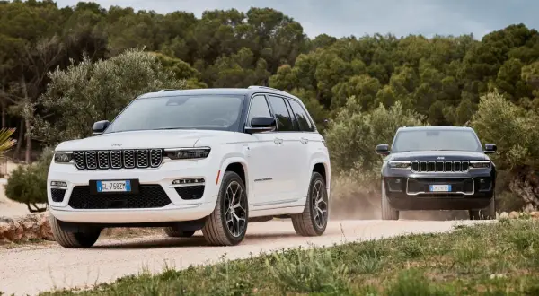 Dwa Jeepy, biały i czarny, jadące po piaszczystej drodze. Jeep kraj pochodzenia to USA, ale te modele wyglądają na europejskie.