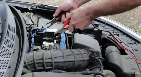 Ręce podłączają kable do akumulatora, by rozwiązać problem nagłego wzrostu spalania diesel.