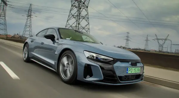 Szary, sportowy Audi GT jedzie po drodze, a w tle widać linie energetyczne i słupy.