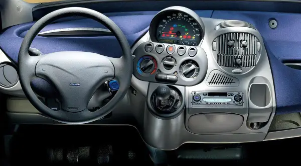 Widok na **fiat multipla wnętrze**: kierownica, deska rozdzielcza z radiem i nawiewami, dźwignia zmiany biegów.