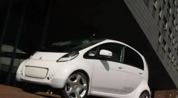Biały, kompaktowy Mitsubishi i-MiEV stoi przed nowoczesnym budynkiem.