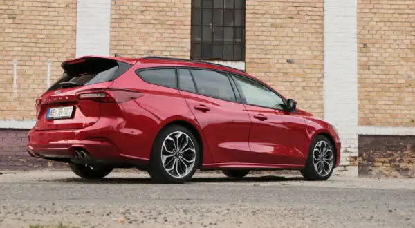 Czerwony kombi Ford Focus, elegancki i sportowy, zaparkowany przy ceglanej ścianie.