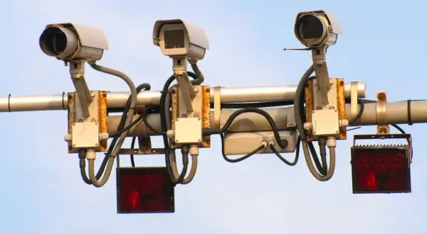 Trzy kamery monitorujące ruch drogowy, każda z migającym **system red light** pod nią.