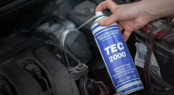Ręka trzyma puszkę TEC 2000, wykonując czyszczenie kolektora dolotowego silnika.