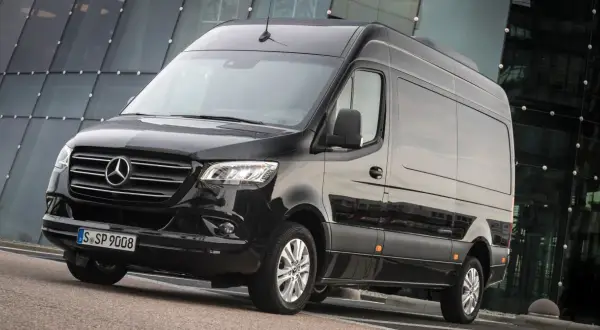 Czarny Mercedes-Benz Sprinter, jeden z najlepszych samochodów dostawczych, zaparkowany przed nowoczesnym budynkiem.