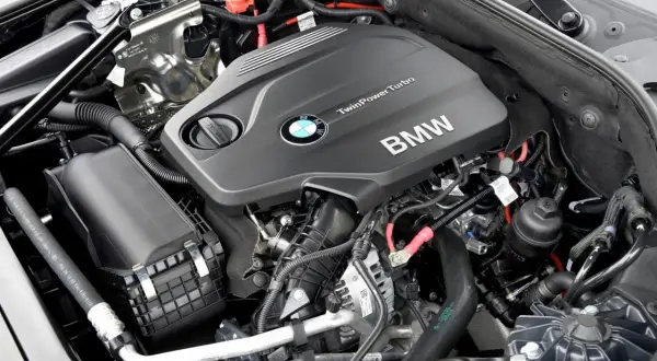 Silniki BMW F10 TwinPower Turbo. Widok na czarny, nowoczesny silnik z logo BMW i licznymi przewodami.