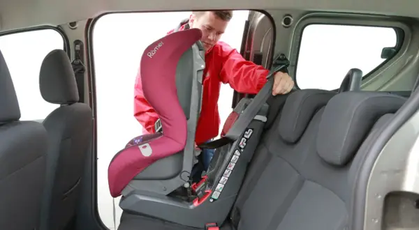 Mężczyzna montuje fotelik dziecięcy. Sprawdź, jak sprawdzić, czy samochód ma isofix, patrząc na zaczepy fotelika.