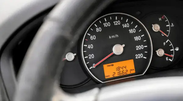 Zbliżenie na deskę rozdzielczą samochodu. Widoczny prędkościomierz, wskaźnik paliwa i temperatury. Cyfrowy wyświetlacz pokazuje przebieg 216621 km.