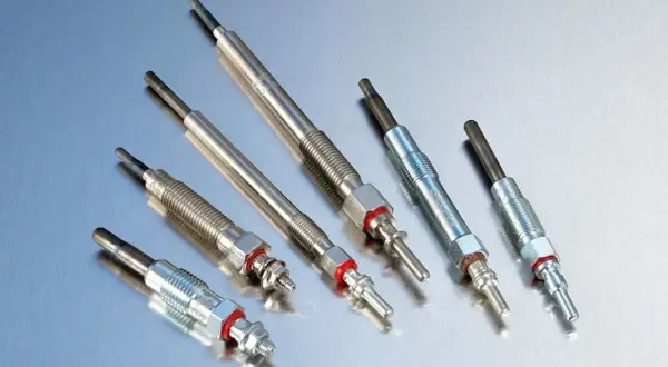 Kilka świec żarowych ułożonych na metalicznej powierzchni. Zepsute świece żarowe objawy mogą być trudne do zauważenia.