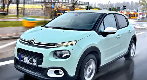 Jasnozielony Citroën C3, jeden z francuskich marek samochodów, jedzie po mokrej drodze.