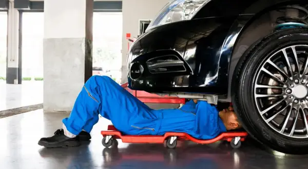 Mechanik pod czarnym autem szuka czujnika położenia wału w Peugeot 207.
