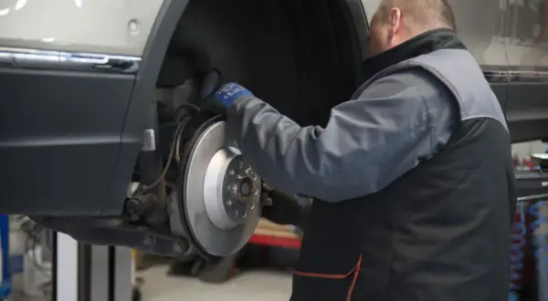 Mechanik sprawdza żywotność klocków hamulcowych przy tarczy hamulcowej samochodu na podnośniku.