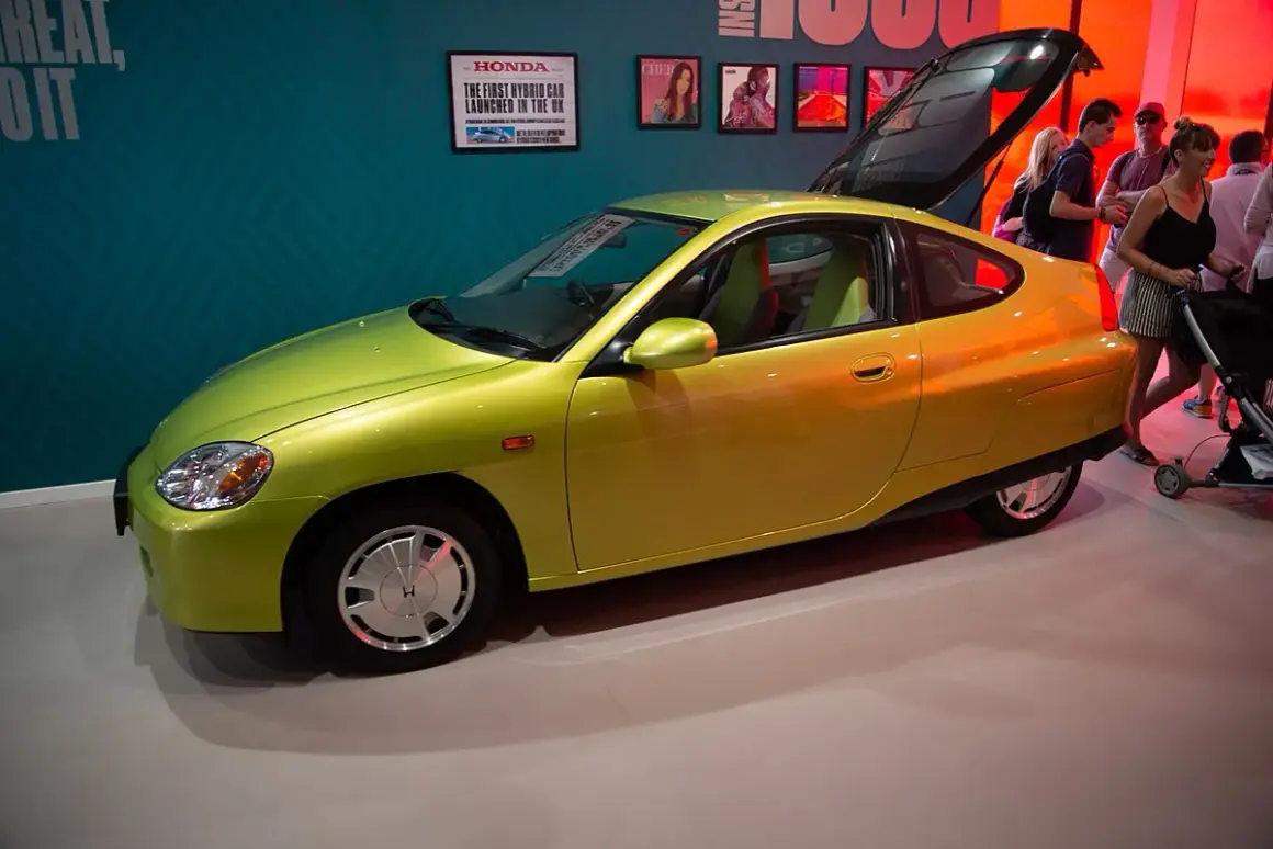 Jasnozielona Honda Insight, pierwsza hybryda na rynku, prezentowana na wystawie. To najlepsza hybryda, która wyznaczyła nowe standardy.