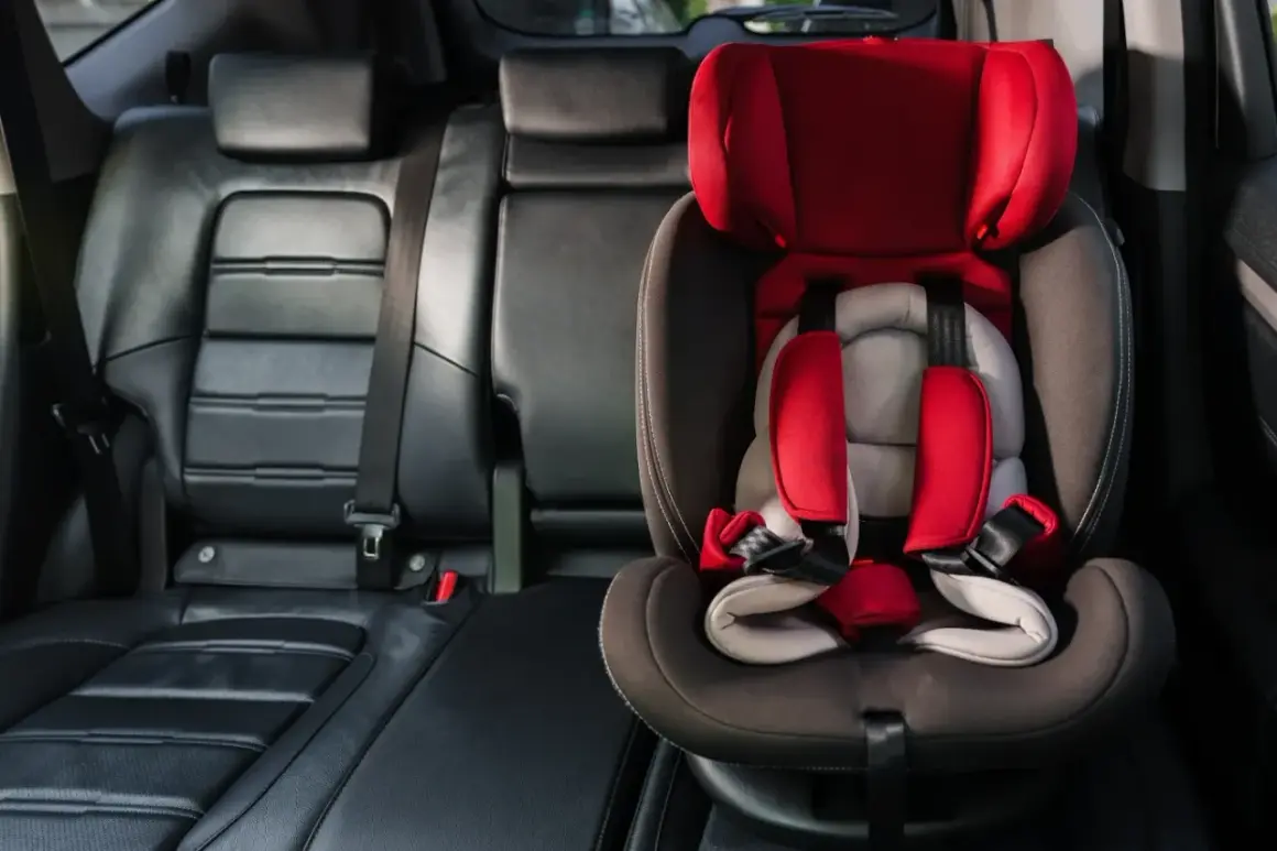 Czerwony fotelik dziecięcy z pasami bezpieczeństwa zamontowany w aucie. System isofix w aucie zapewnia bezpieczne podróżowanie najmłodszych.
