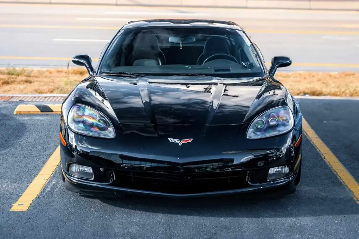 Błyszczący, czarny Chevrolet Corvette, ikoniczna amerykańska marka samochodów, zaparkowany na tle żółtych linii.