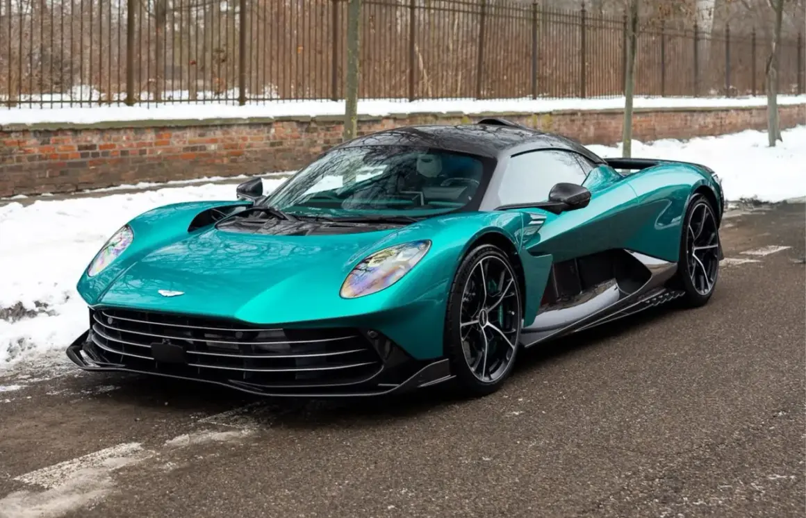 Turkusowy Aston Martin, prawdopodobnie najdroższe auto w Polsce, na tle zimowego krajobrazu z ceglanym murem i płotem.